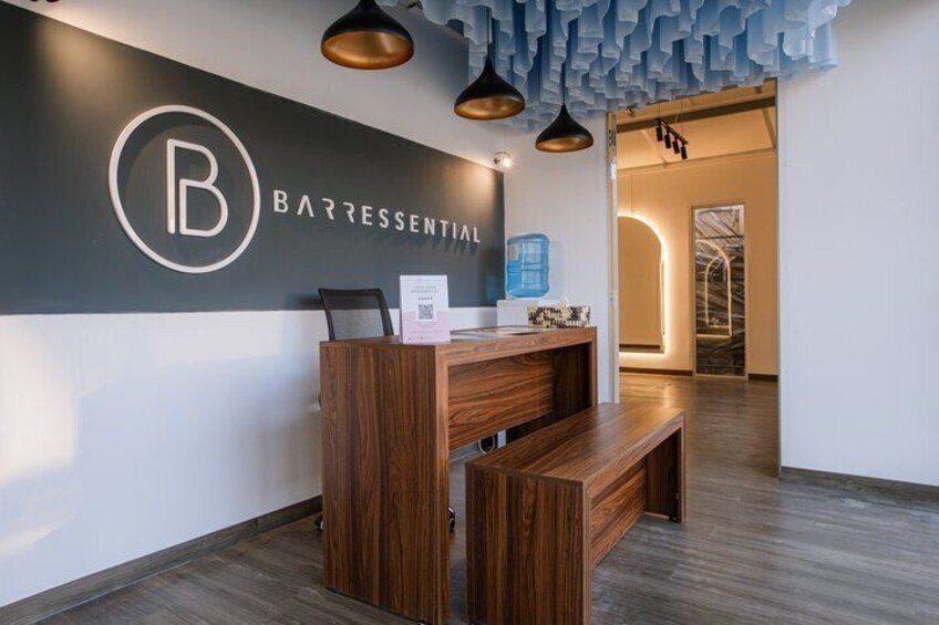 A reception desk with a wooden finish, a logo on the wall, and pendant lighting. 1