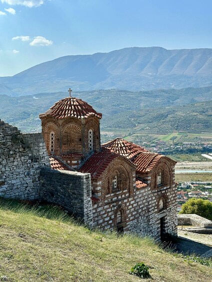 A historic church with a red-tiled roof and stone walls, surrounded by a mountainous landscape. 4