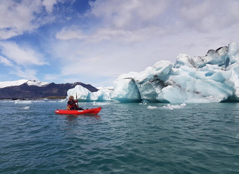 A person kayaking on calm waters with large icebergs and mountains in the background. 5