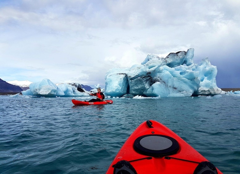A person kayaking in front of large icebergs in a body of water. 4