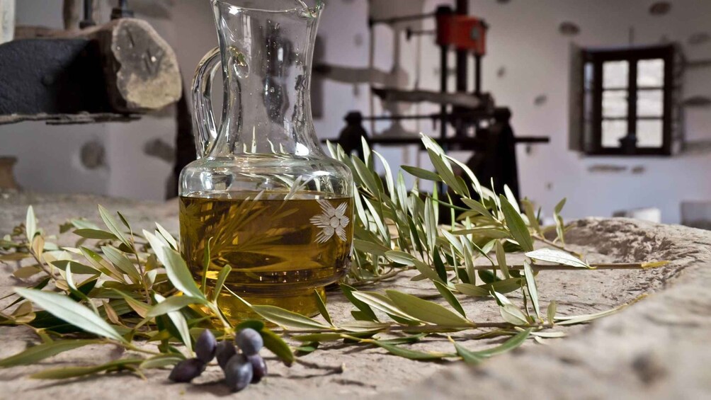 A glass bottle with olive oil, olive branches, and olives on a stone surface. 3