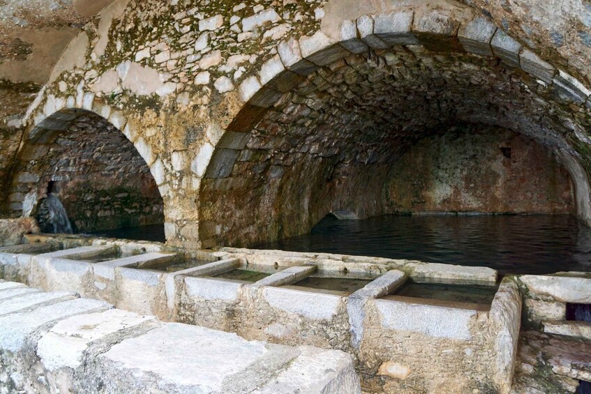 An ancient stone structure with arched passageways and a water feature. 4
