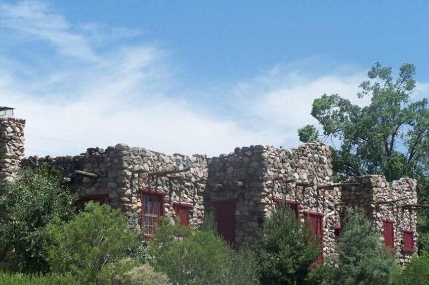 A stone building with red window shutters, surrounded by greenery. 1
