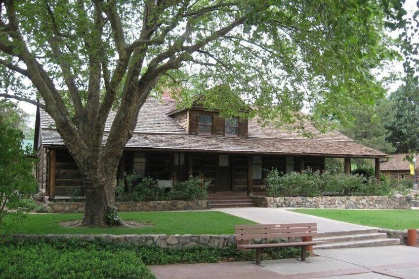 A rustic log cabin with a stone foundation, surrounded by a well-maintained lawn and a large tree. 4