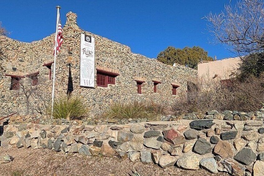 A stone building with a flag, a sign, and a rocky foreground. 2