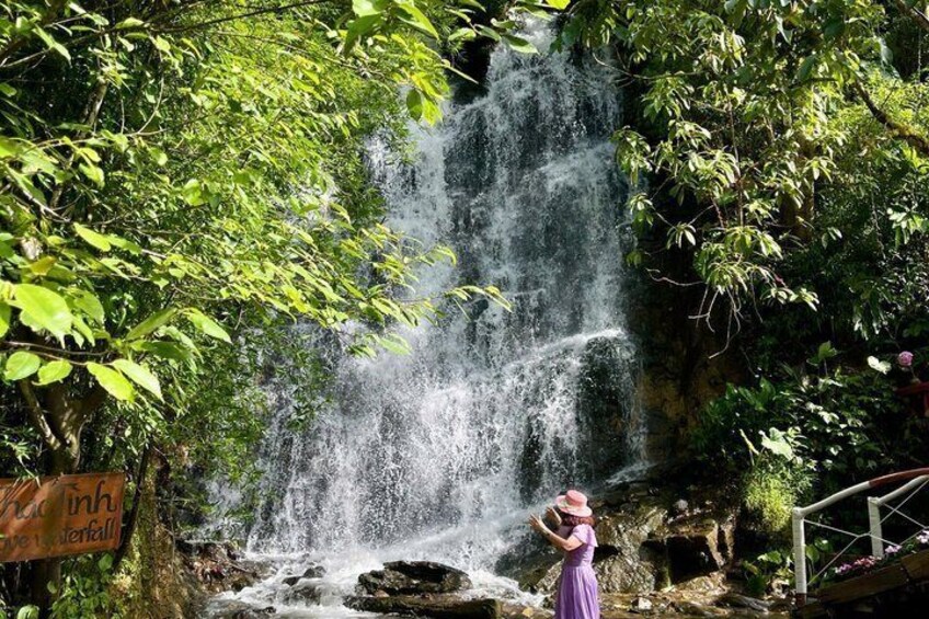 A waterfall surrounded by lush greenery and a person in a purple dress. 4