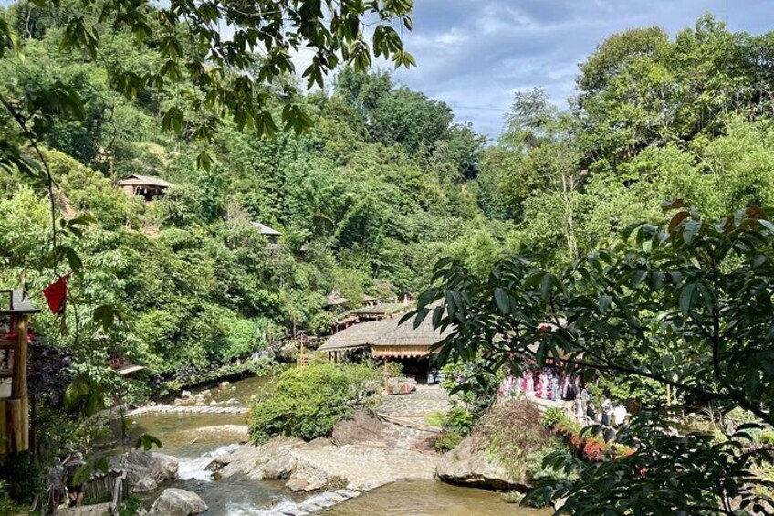 A river flowing through a lush, green landscape with traditional huts and a thatched-roof structure. 3