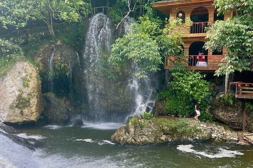A waterfall, a wooden building, and a person standing on rocks. 3