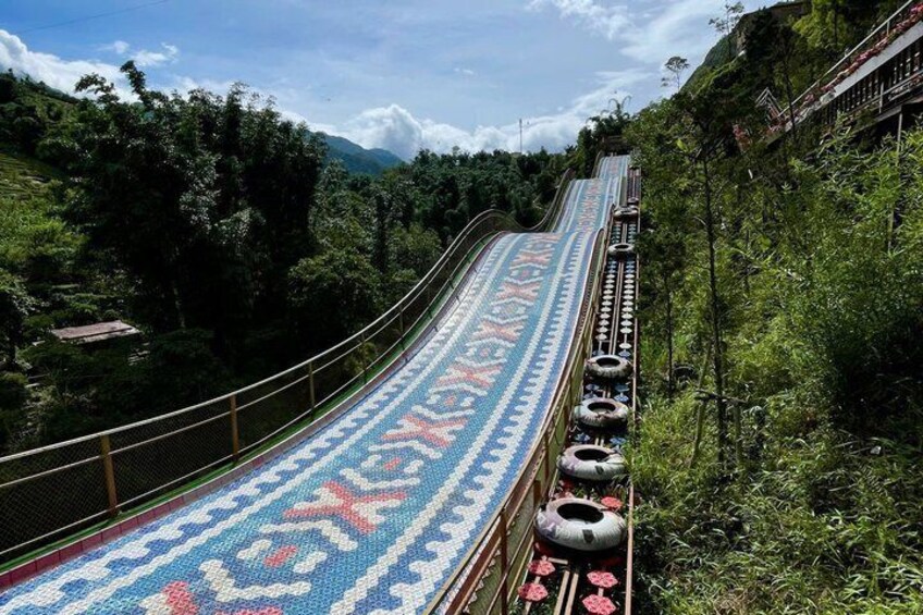 A long, narrow, elevated walkway with a patterned carpet, surrounded by lush greenery and mountains in the background. 2