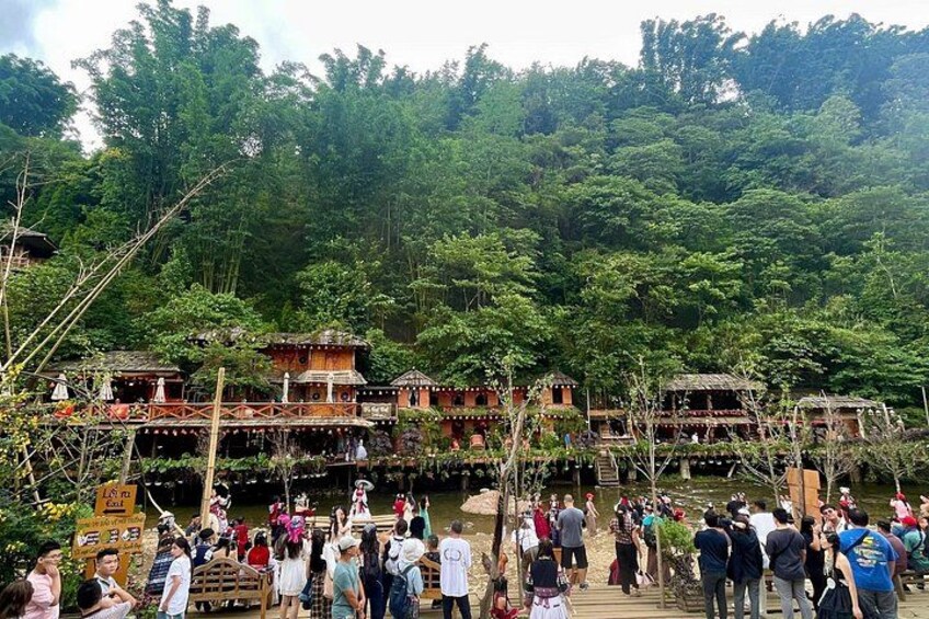 A group of people on a wooden bridge over a river, surrounded by lush greenery and traditional buildings. 5