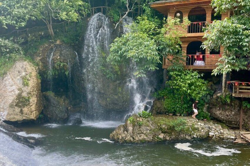 A waterfall, a wooden building, and a person standing on rocks. 5