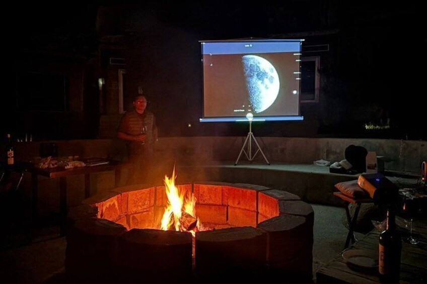 A fire pit with flames, a person in the background, and a screen displaying a moon. 1