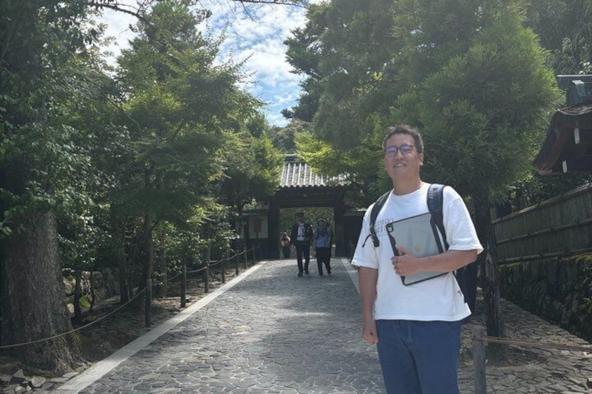 A person standing on a cobblestone path with trees and a traditional structure in the background. 2