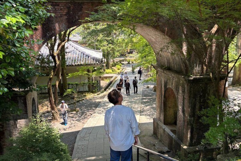 A person walking on a stone pathway in a traditional garden with trees and a bridge. 3