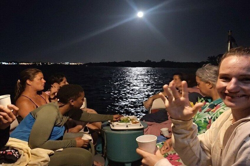 A group of people on a boat at night with a moonlit background. 3