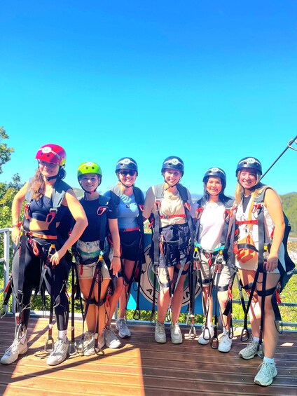A group of people on a wooden deck with safety harnesses, wearing helmets, and standing outdoors. 3