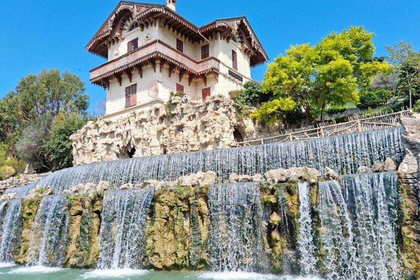 A building with a stone base and a wooden upper structure, a cascading waterfall, and a tree with yellow leaves. 2