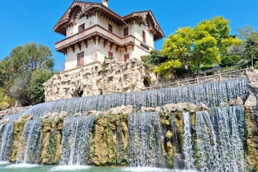 A historic building with a stone facade and a waterfall in front. 2