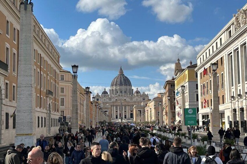 A crowded square with historic buildings and a prominent dome in the background. 1