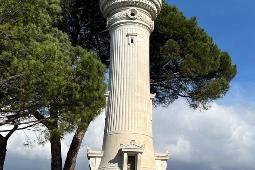 A tall, white column with a clock, surrounded by trees. 2