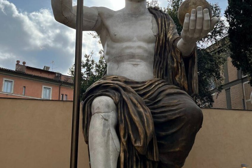 A statue of a muscular figure holding a sphere, with draped clothing and a visible knee joint. 4