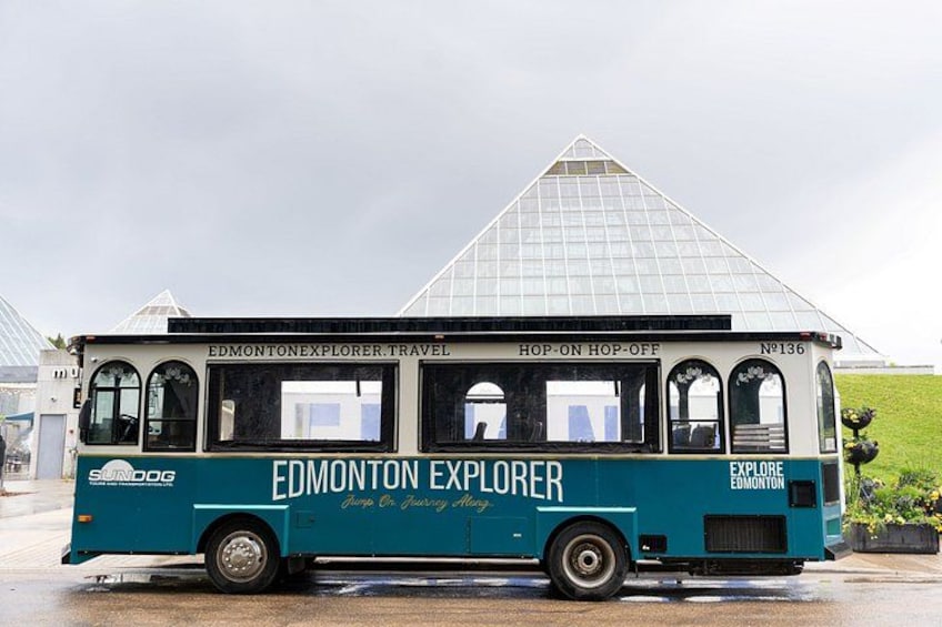 A tour bus with 'Edmonton Explorer' branding parked in front of a glass pyramid. 1