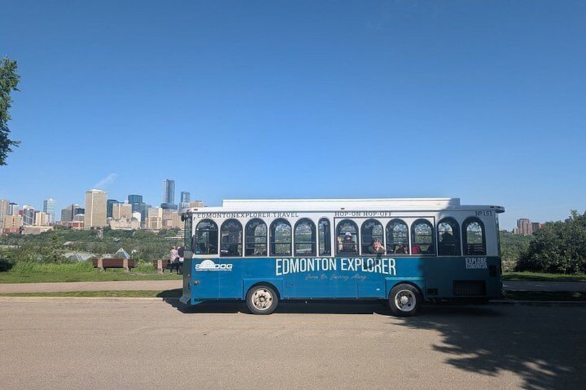 A blue bus with 'Edmonton Explorer' written on it, parked on a road with a city skyline in the background. 2
