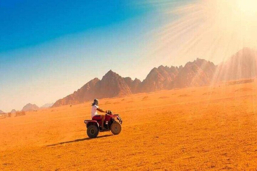 A person riding a red quad bike in a desert with mountains in the background. 4