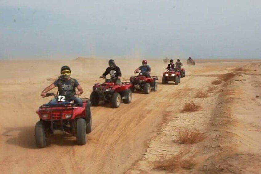 A group of people riding quad bikes on a sandy path in a desert. 1
