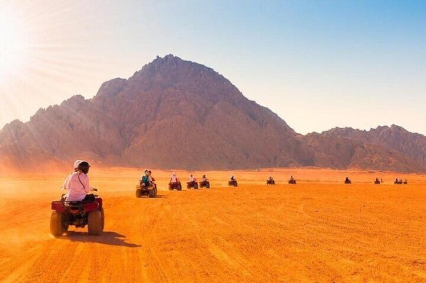 A group of people riding quad bikes across a desert landscape with mountains in the background. 5