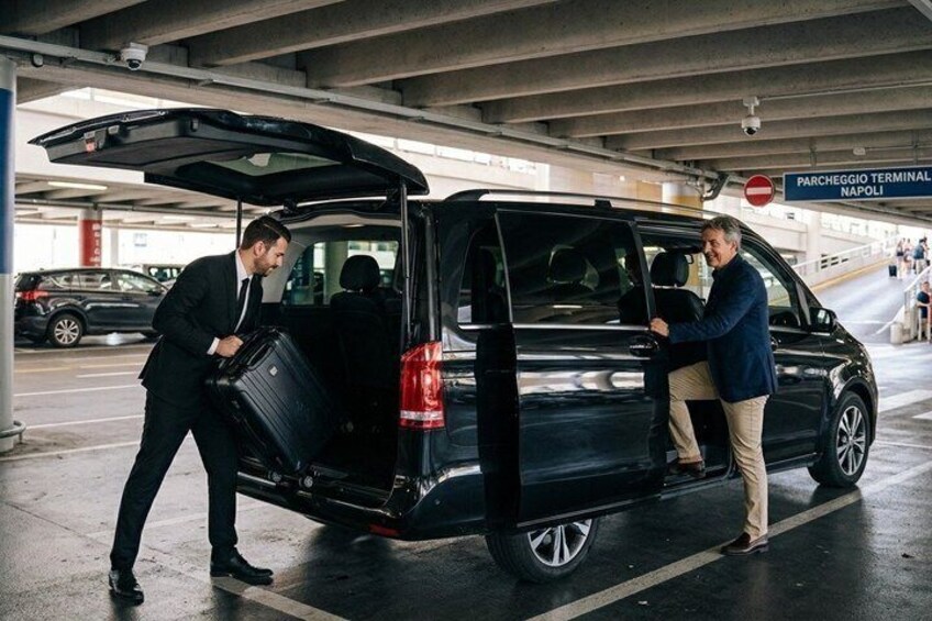 Two men unloading luggage from a black van at a parking garage. 3