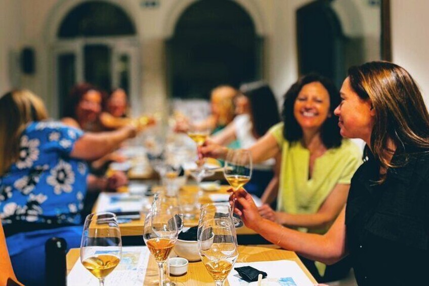 A group of people seated at a long table, toasting with wine glasses. 2