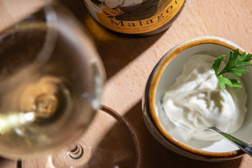 A glass of white wine, a bowl of yogurt with a parsley garnish, and a bottle of Malazez wine. 1