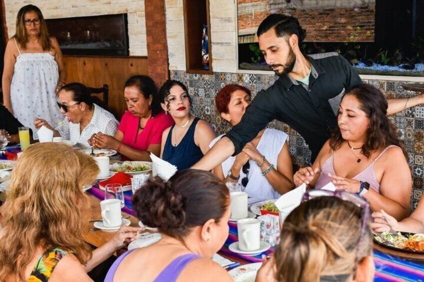 A group of people dining at an outdoor restaurant with a tiled wall and a brick oven in the background. 4