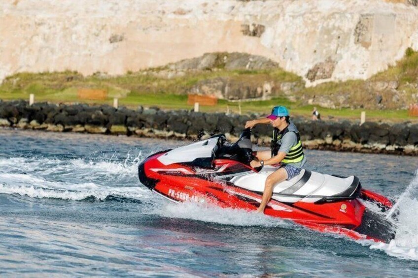 A person riding a red and white jet ski on water with a rocky shoreline in the background. 5