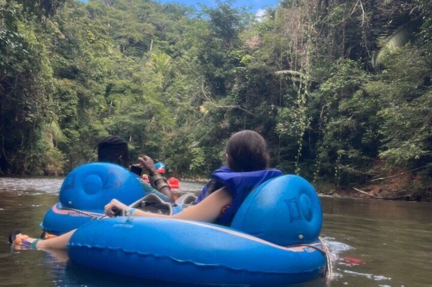 Two people on a blue inflatable raft in a river surrounded by dense greenery. 2