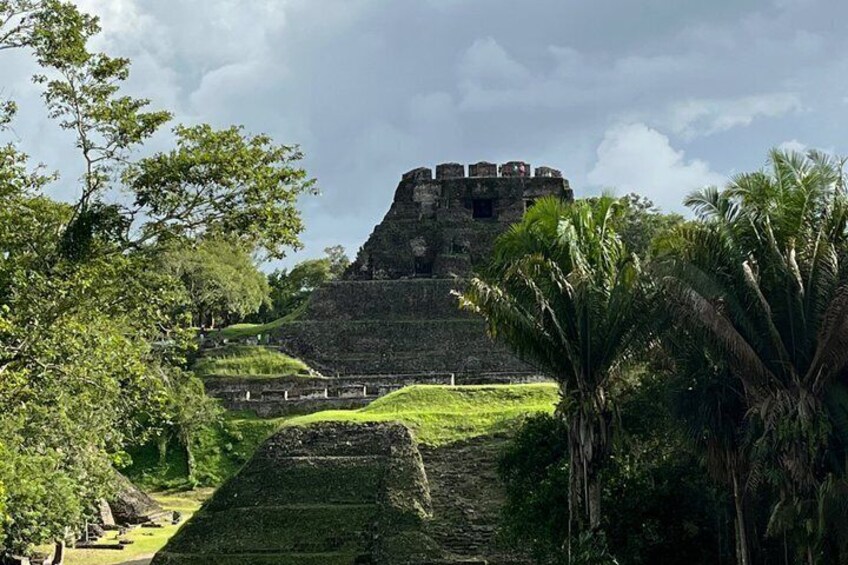 A large ancient pyramid with a smaller structure on top, surrounded by lush greenery and palm trees. 1