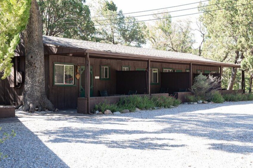 A wooden cabin with a porch, surrounded by trees and gravel. 2