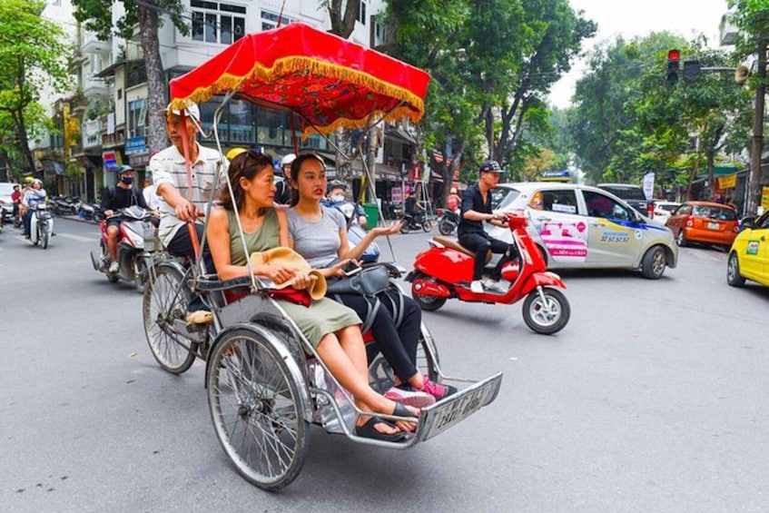 A person in a wheelchair being pushed by another individual on a street with other vehicles and pedestrians. 3