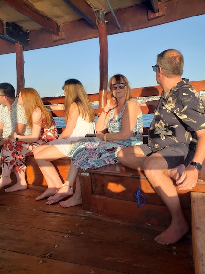 A group of people sitting on a wooden bench on a boat, with a clear sky and water in the background. 4