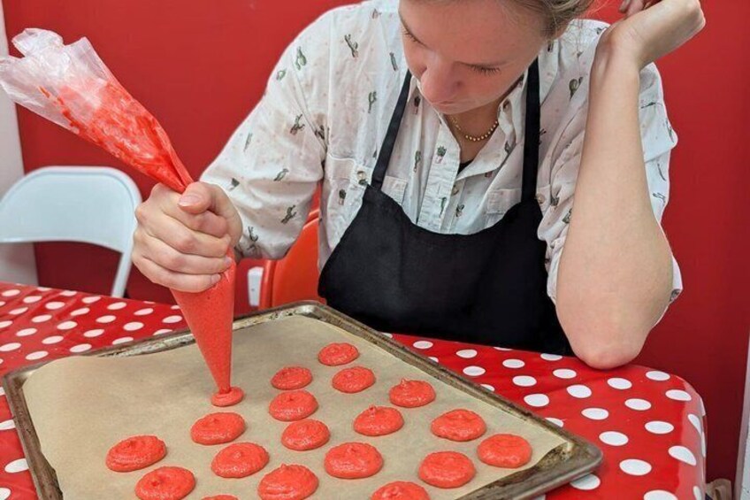 A person piping red icing onto cookies on a baking sheet. 2