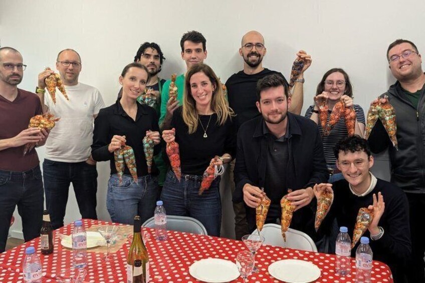 A group of people at a table with a red and white polka dot tablecloth, holding various types of sausages. 3