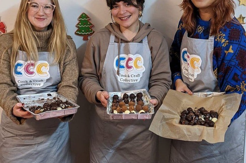 Three individuals wearing aprons with logos, holding trays of food items. 5
