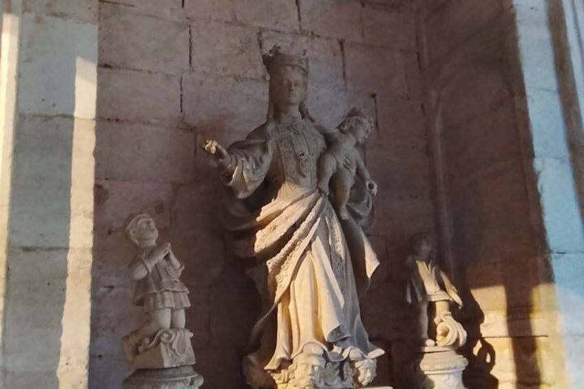 A stone statue of a robed figure with a child, set against a stone wall. 5