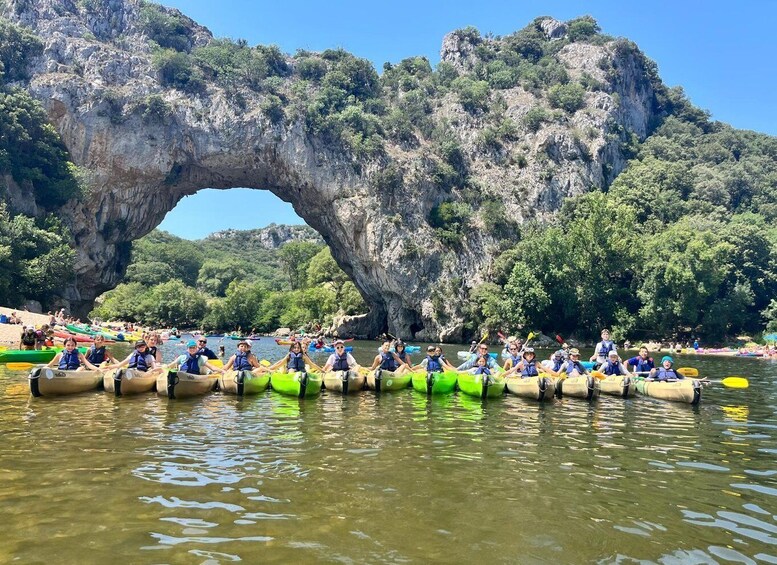 A group of people in kayaks lined up in front of a large rock arch. 3