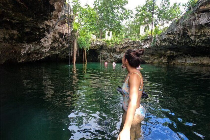 A woman in a swimsuit standing in a clear water body surrounded by rocky cliffs and greenery. 2