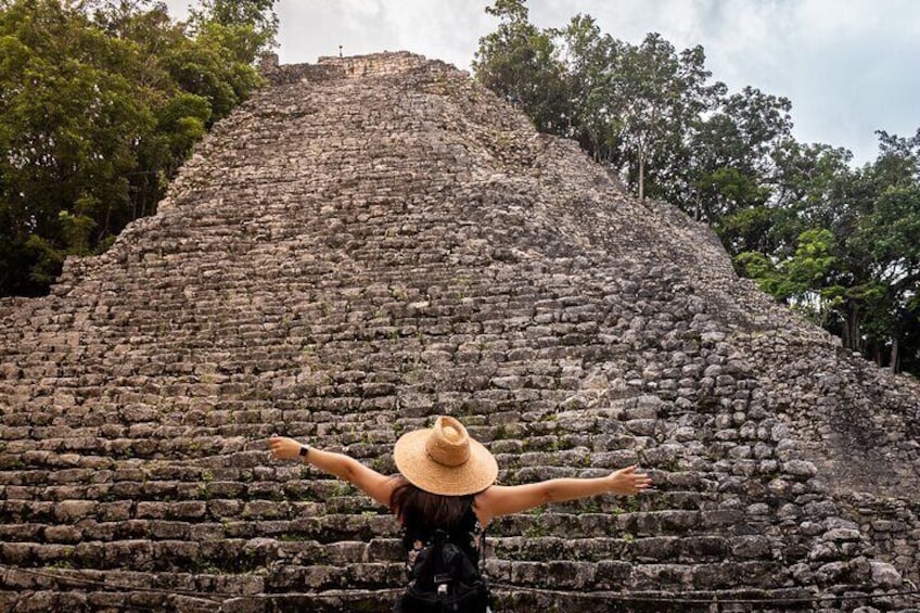 A person standing in front of a large stone pyramid with arms outstretched. 5