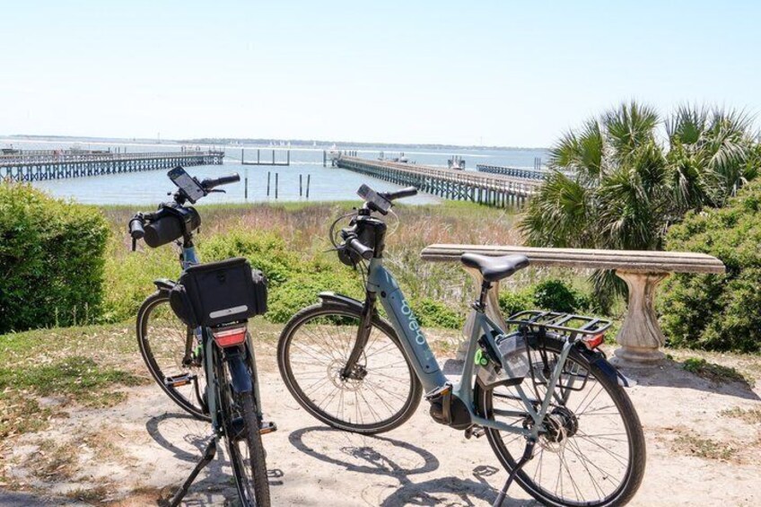 Two bicycles parked on a sandy path with a view of a pier and the sea in the background. 3