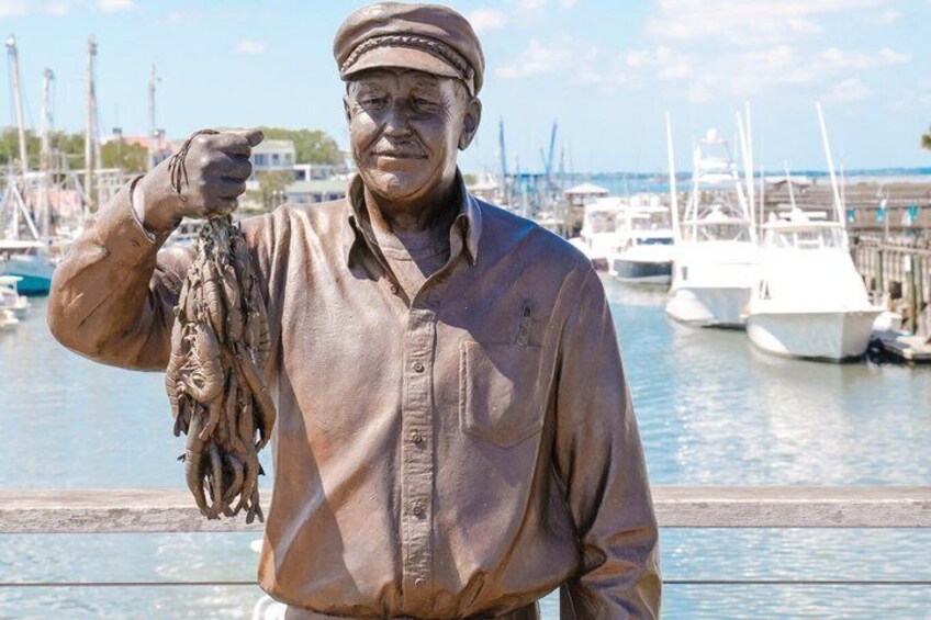 A statue of a man holding fish, with boats and a marina in the background. 5