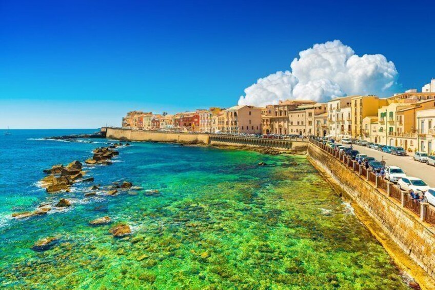 A coastal town with clear turquoise waters, a stone wall, and colorful buildings. 2